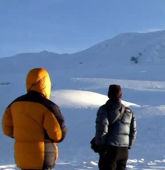 Two climbers gazing up at the snowy summit of Mera Peak under the early morning light.