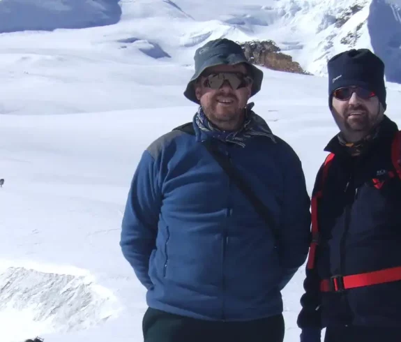 Two trekkers posing in front of the snowy slopes of Mera Peak with other climbers in the background.