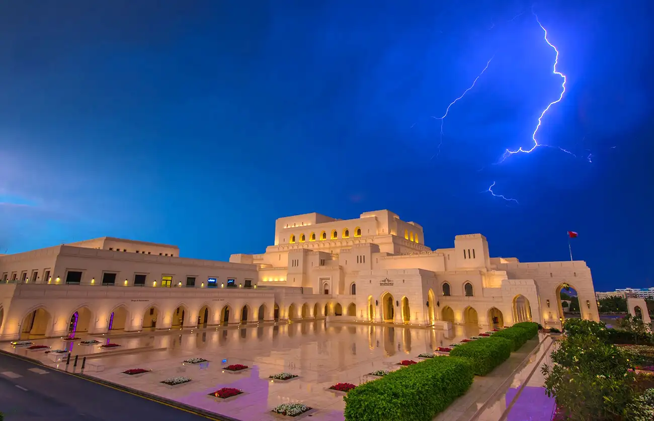 Lightning illuminates the sky above the Royal Opera House in Muscat, Oman, creating a striking contrast against the building's elegant architecture.