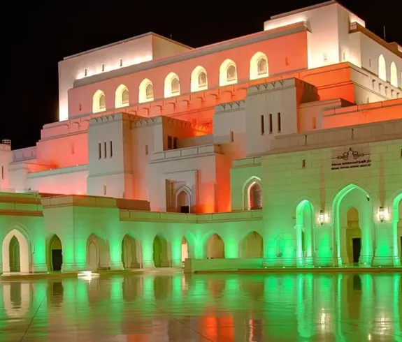 Royal Opera House Muscat illuminated at night in vibrant green and orange lights, showcasing its grand architectural design.