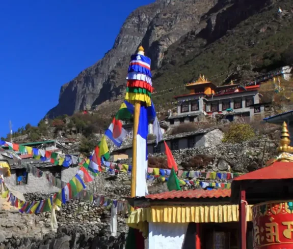 Colorful prayer flags and traditional buildings in Thamo Village, nestled in the mountainous terrain of Sagarmatha National Park, Nepal.