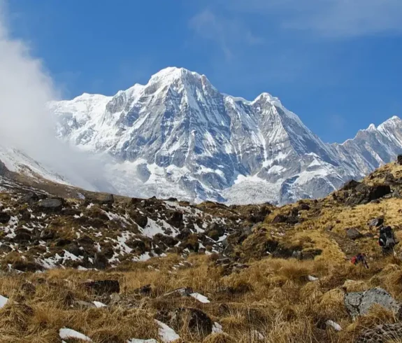 Trekkers walking through rugged terrain towards Annapurna Base Camp with snow-capped mountains in the background in the Annapurna Conservation Area, Nepal.