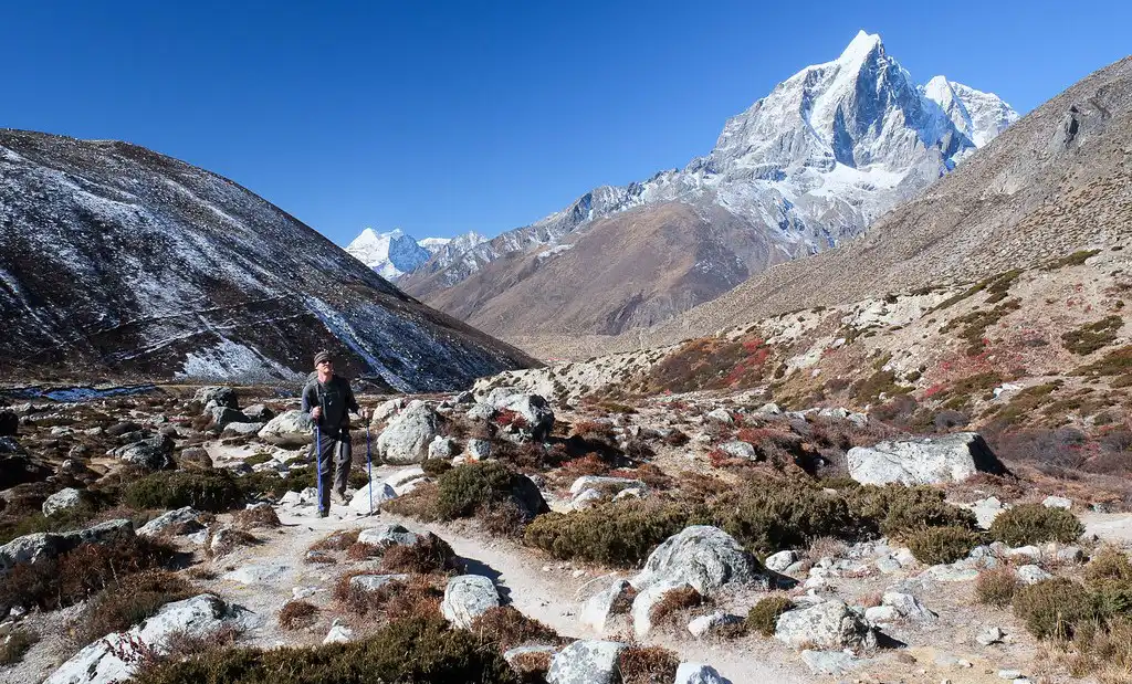 A trekker on a trail in the Himalayas with a snow-capped mountain in the background.
