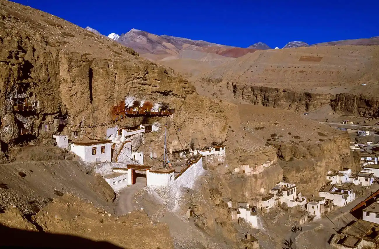 Het Tsegu-rotsklooster is gebouwd in de ruige klifwand, omgeven door dor, bergachtig terrein onder een helderblauwe lucht.