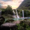 A serene view of Wadi Darbat in the Dhofar Governorate, featuring cascading waterfalls, lush greenery, and tranquil turquoise waters at sunset.