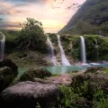 A serene view of Wadi Darbat in the Dhofar Governorate, featuring cascading waterfalls, lush greenery, and tranquil turquoise waters at sunset.