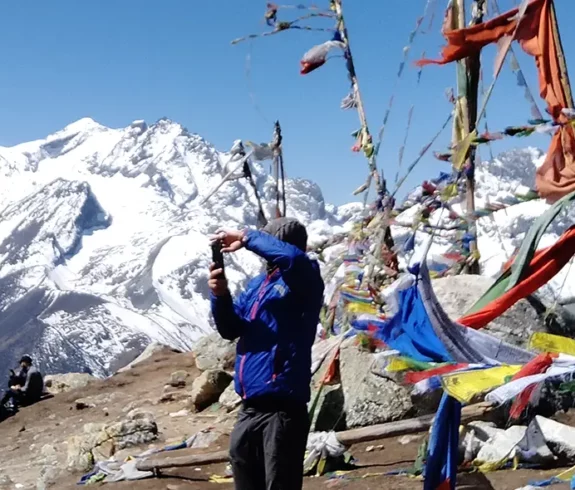 Trekker capturing the stunning snow-covered mountains in Langtang, Nepal, surrounded by colorful prayer flags.