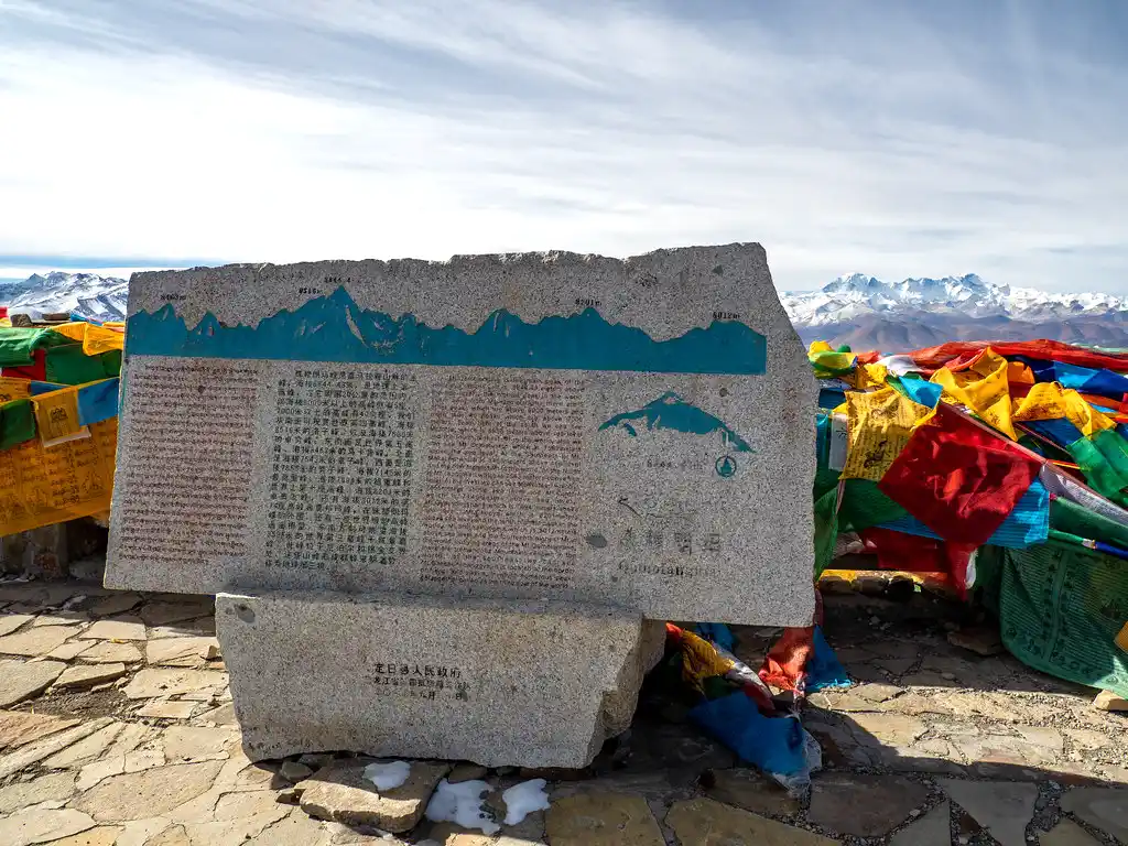 Gawula Pass stone monument with Tibetan prayer flags and snowy mountains in the background.