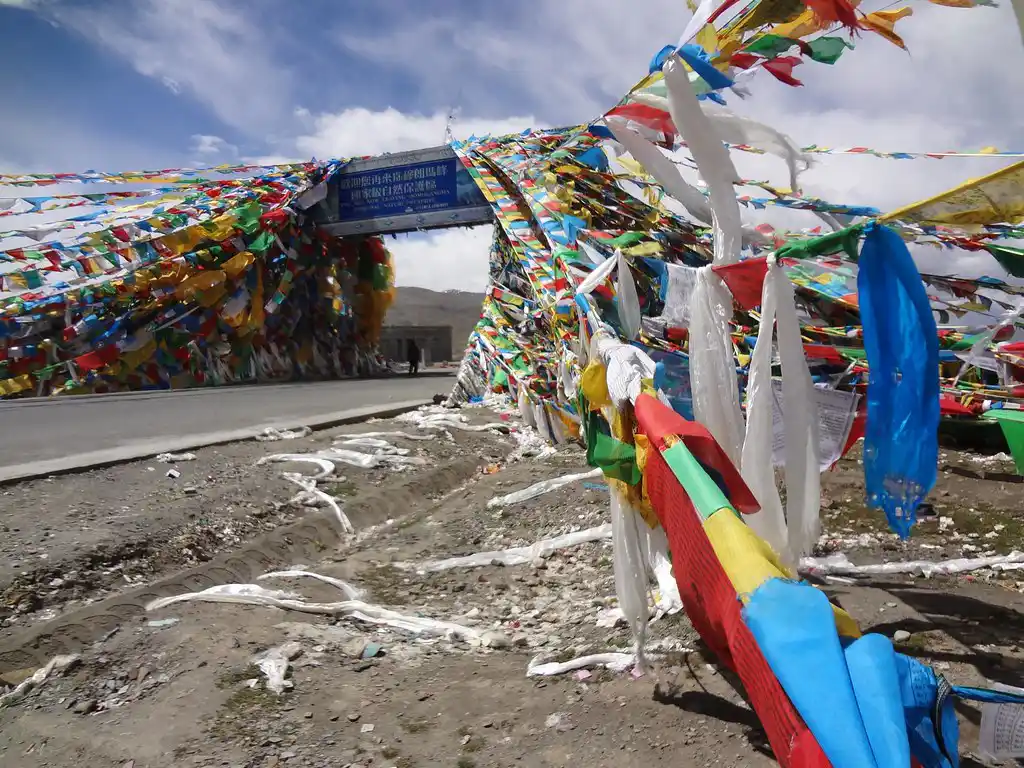 Colorful Tibetan prayer flags at Gyatso La Pass with a road sign in the background.