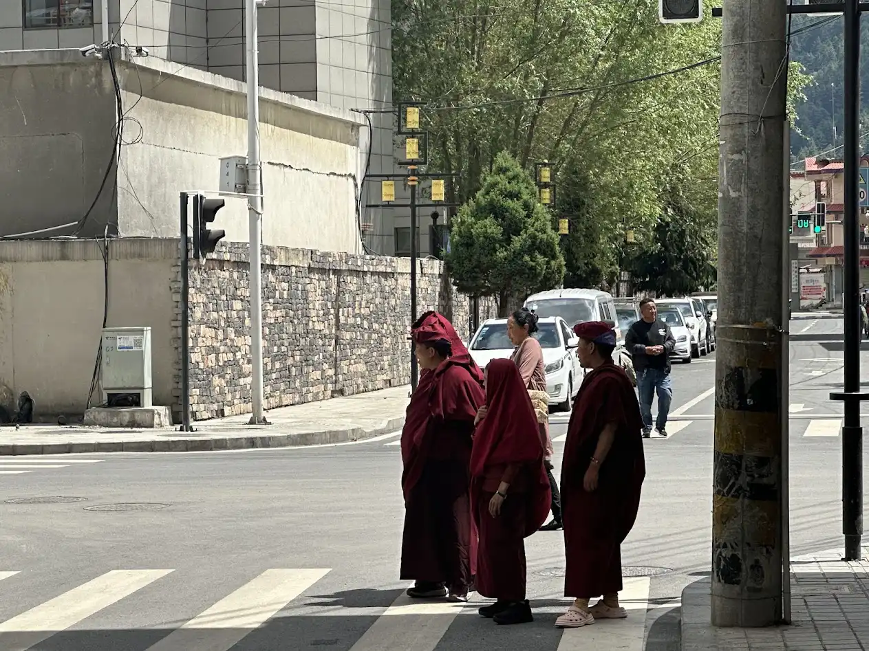 Three Tibetan monks in red robes stand at a crosswalk in Gyirong, near the Nepal–Tibet border.