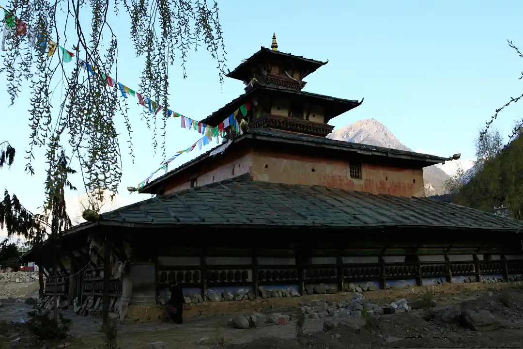 Paba Temple in the serene Himalayan landscape with colorful prayer flags hanging in the trees.