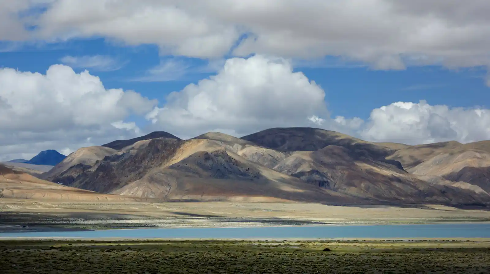 Pelku Tso Lake with barren mountains under a cloudy sky in western Tibet.