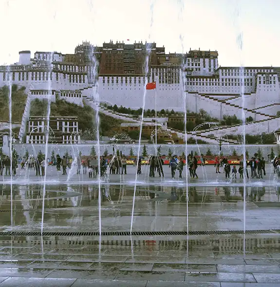 Potala Palace in Lhasa, Tibet, standing tall above the city with dramatic mountain and cloud backdrop.