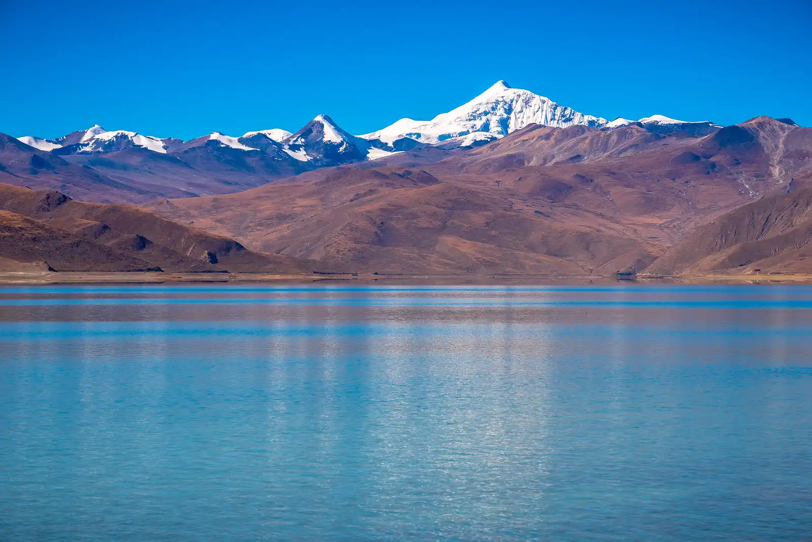 Clear blue waters of Yamdrok Lake with snow-capped mountains in the background.