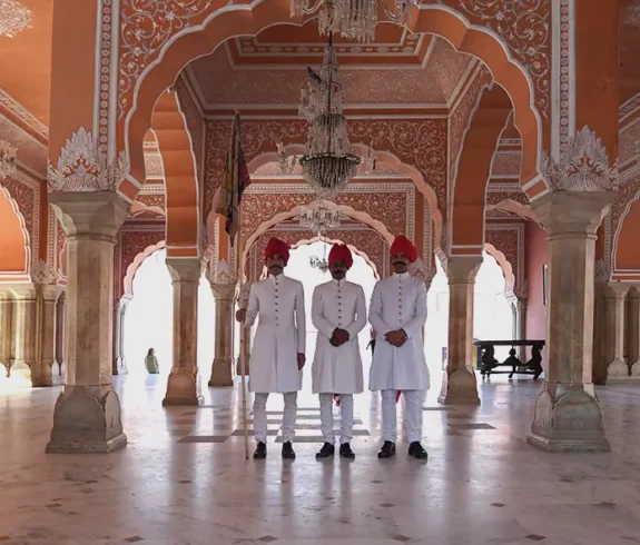 A lavish interior hall in the City Palace Museum, Jaipur, adorned with intricate gold, red, and green mirror work and vibrant floral patterns on its arches and walls.