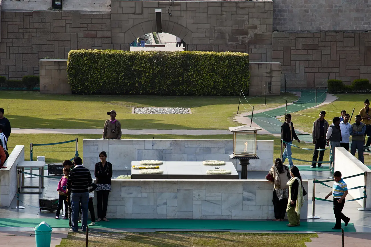 A view of the Raj Ghat memorial in Delhi, showing the black marble platform with flower offerings, the eternal flame, and visitors observing the site.