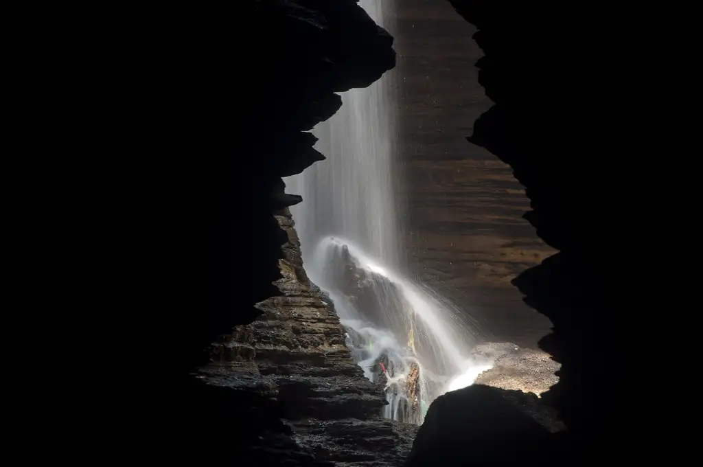 Waterfall from Devi's Falls cascading into the dark limestone depths of Gupteswor Mahadev Cave in Pokhara, Nepal.