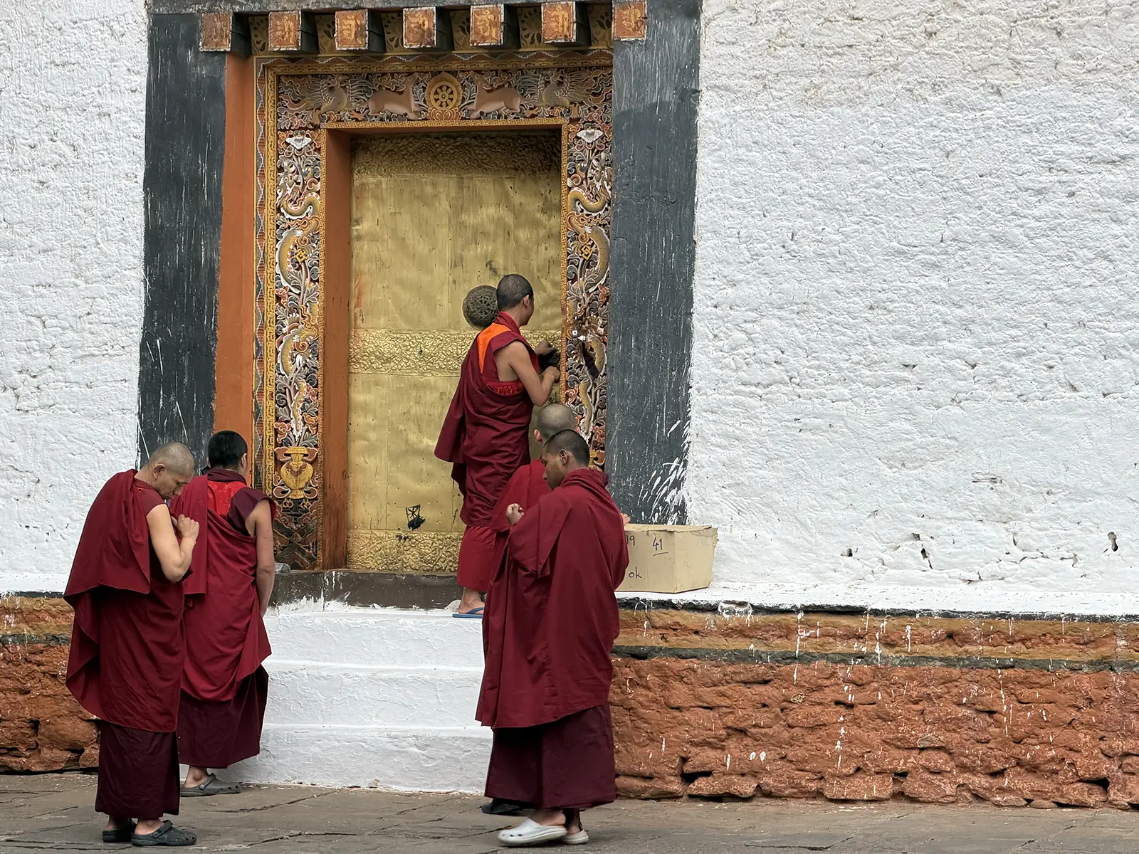 Buddhist monks in maroon robes at the gilded entrance of Punakha Dzong, Bhutan