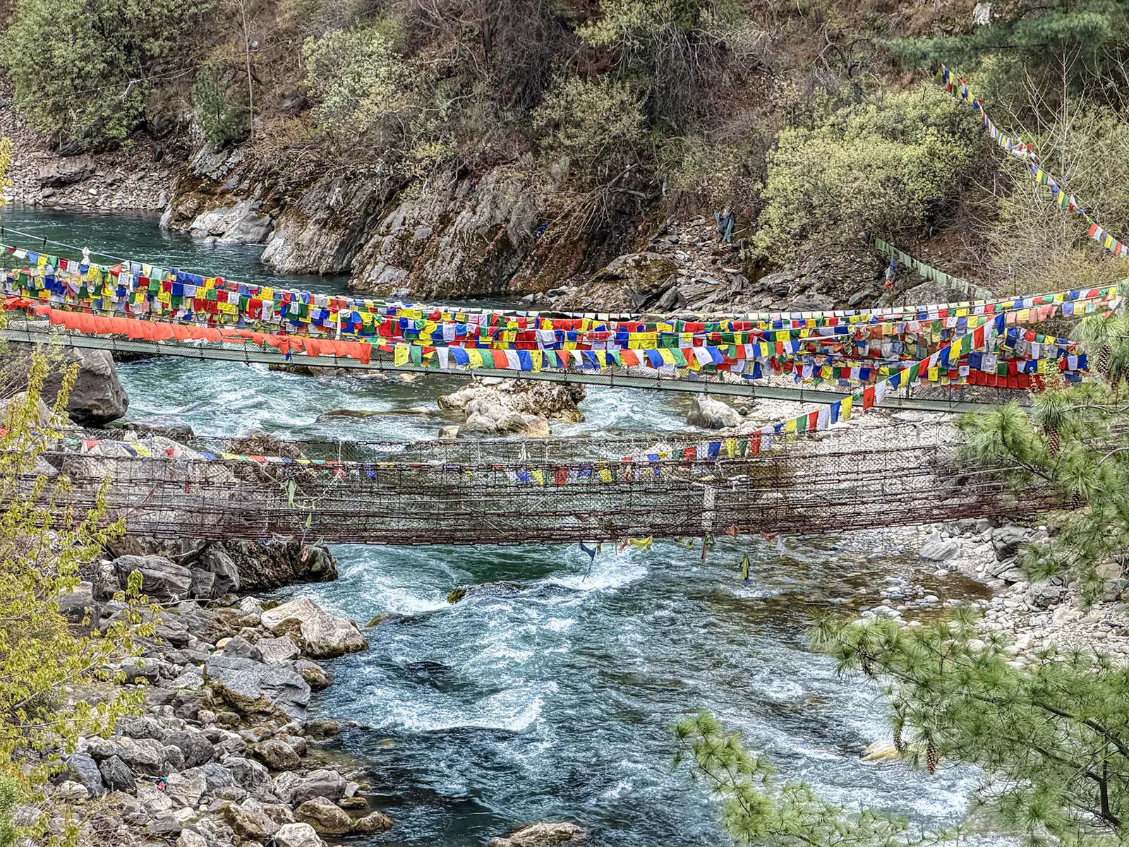 Wang Chhu River with prayer flags strung across iron suspension bridge near Thimphu Bhutan