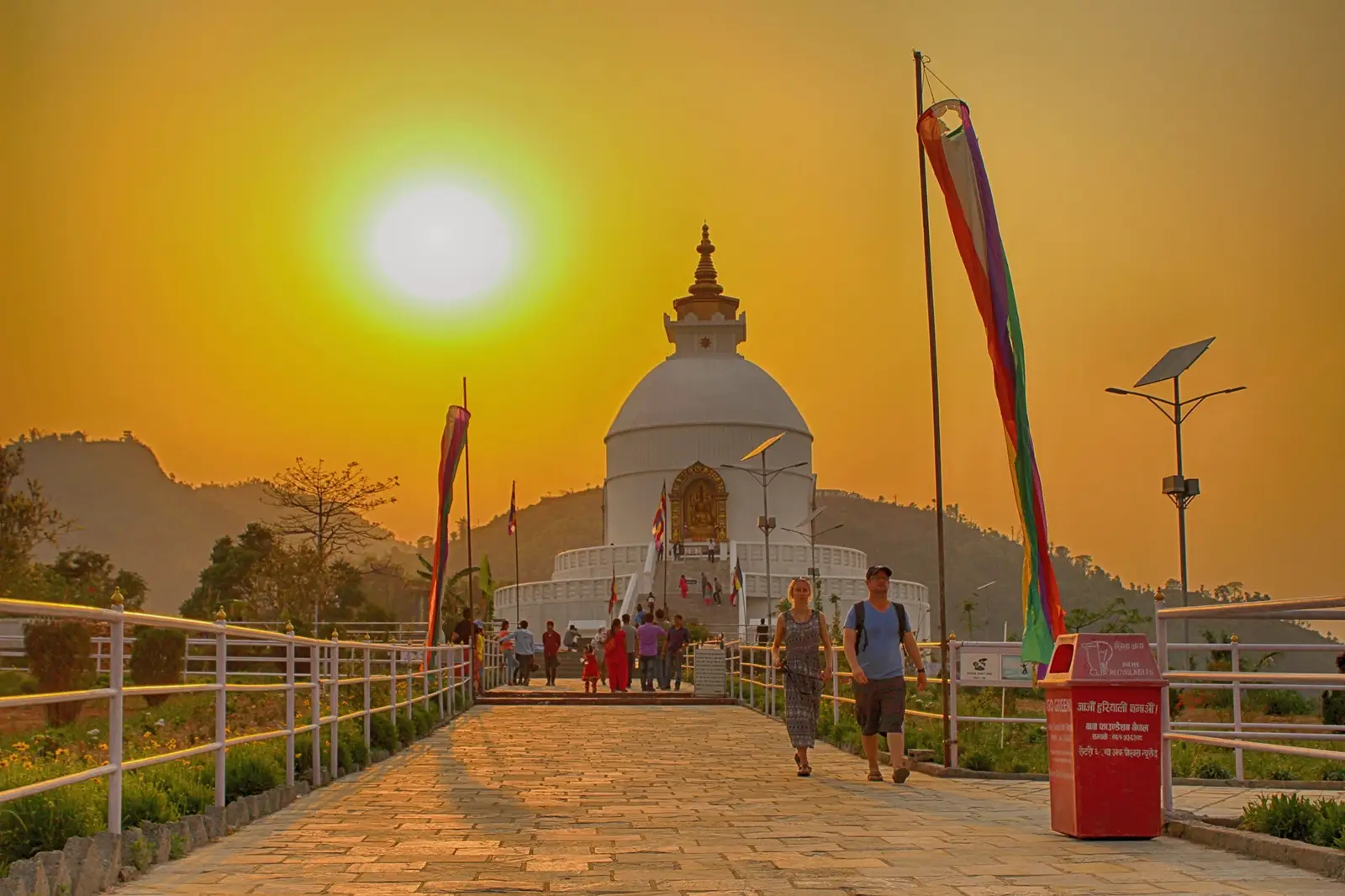 The white dome of the World Peace Pagoda (Shanti Stupa) in Pokhara, Nepal, illuminated by a warm, golden sunset.