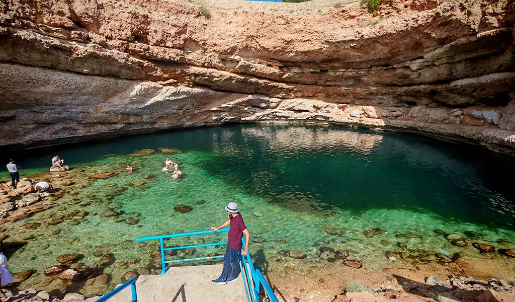 Bimmah Sinkhole in Oman with crystal-clear turquoise water, rocky cliffs, and visitors swimming in the natural pool.