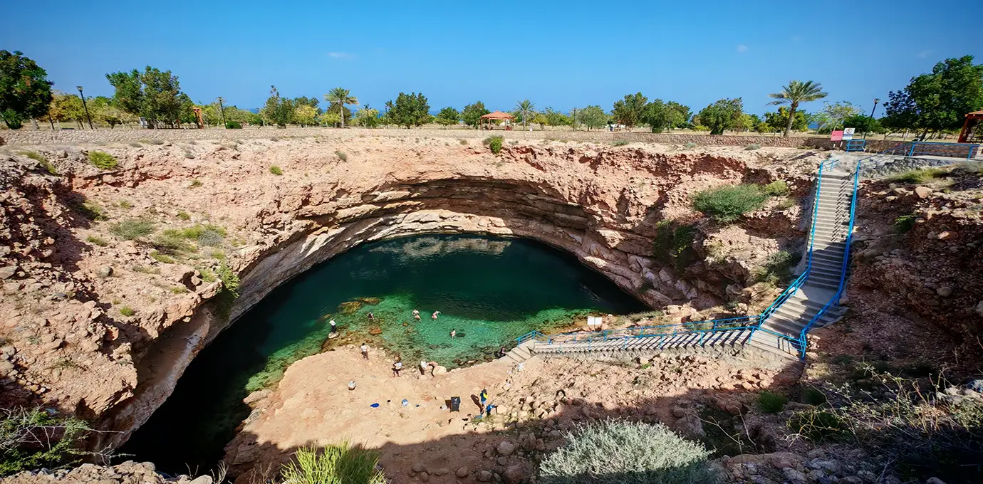 A large limestone sinkhole with turquoise water at Bimmah Sinkhole in Oman.