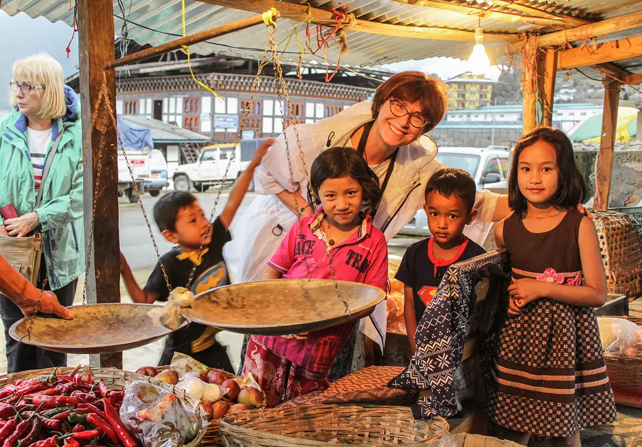 Smiling tourist with Bhutanese children at a local market stall.