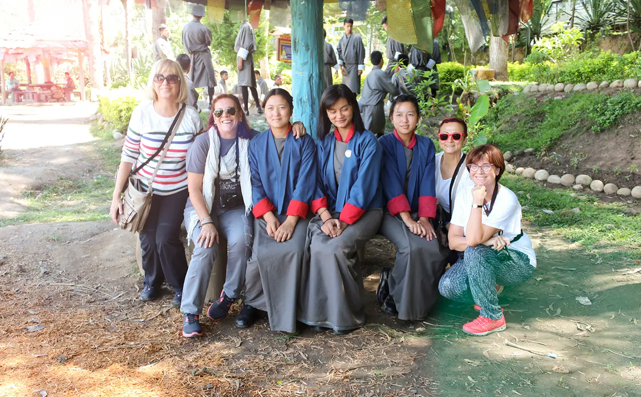 Tourists and Bhutanese schoolgirls posing together under prayer flags.
