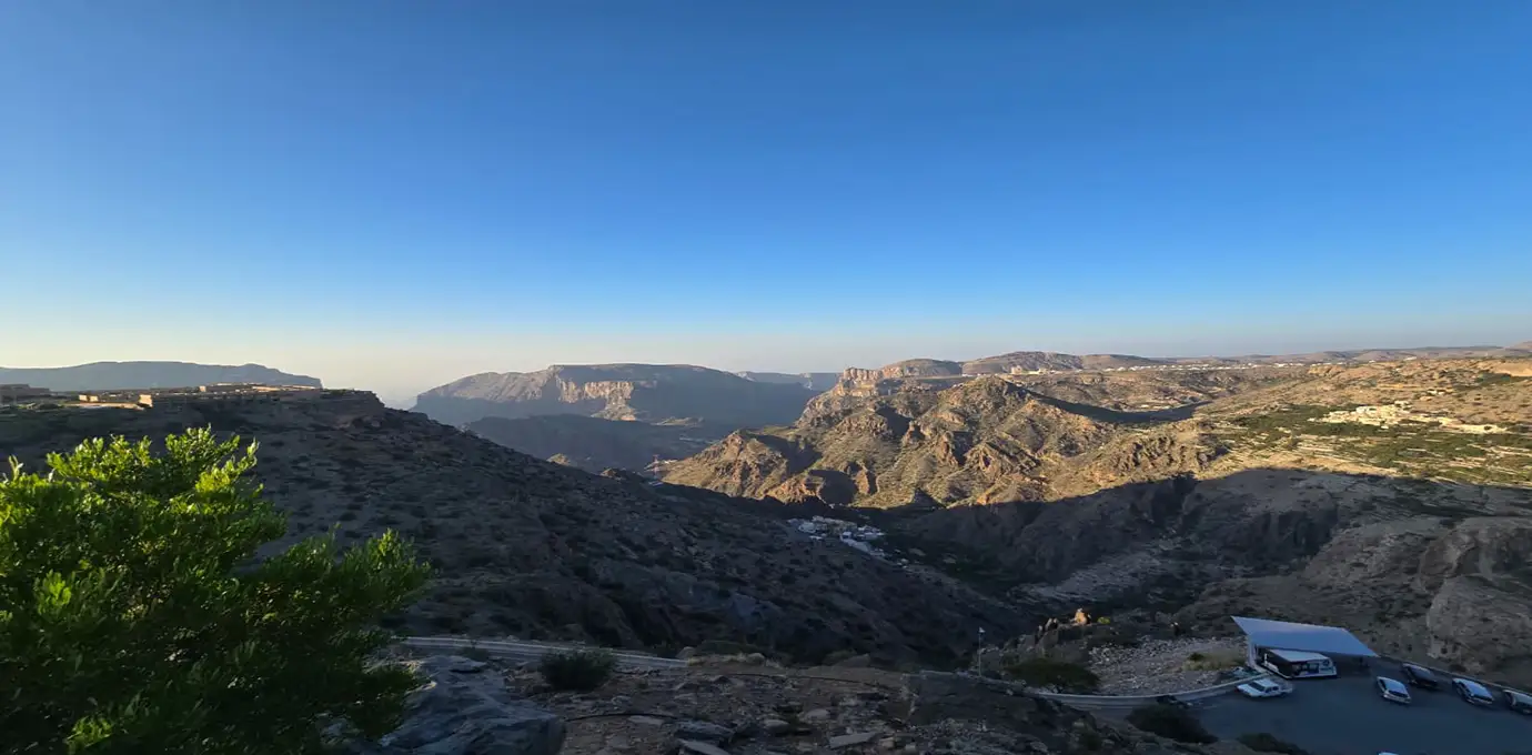 View of Jabal Akhdar’s rugged mountains and deep canyons under a clear blue sky, with terraced villages and winding roads below.