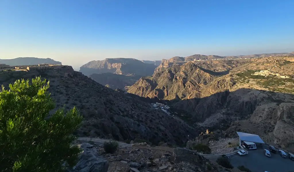 Mountain landscape of Jabal Akhdar in Oman with deep valleys, rocky cliffs, and winding roads under a clear blue sky.