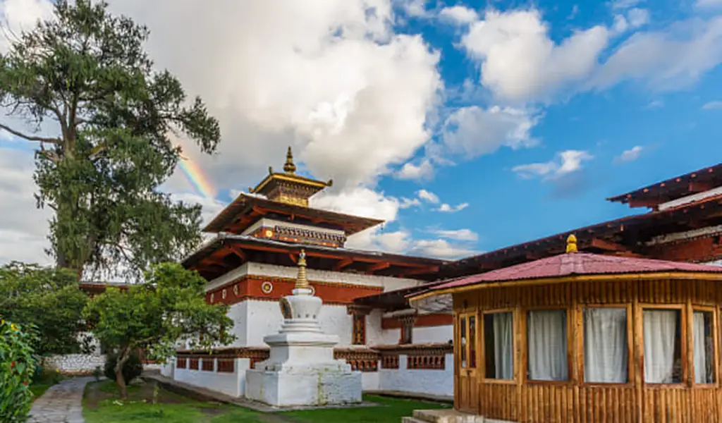 Kyichu Lhakhang temple in Paro, Bhutan, with whitewashed walls, ornate red-and-gold roofs, and a small white stupa in a green courtyard.