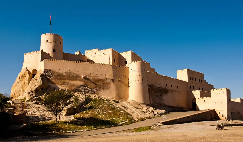Nakhal Fort in Oman perched on a rocky hill, featuring strong fortress walls and towers under a clear blue sky.