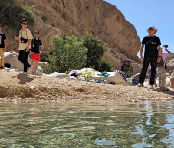 Visitors enjoying the clear natural pools of Wadi Bani Khalid in Oman, surrounded by rocky canyon walls and desert scenery.