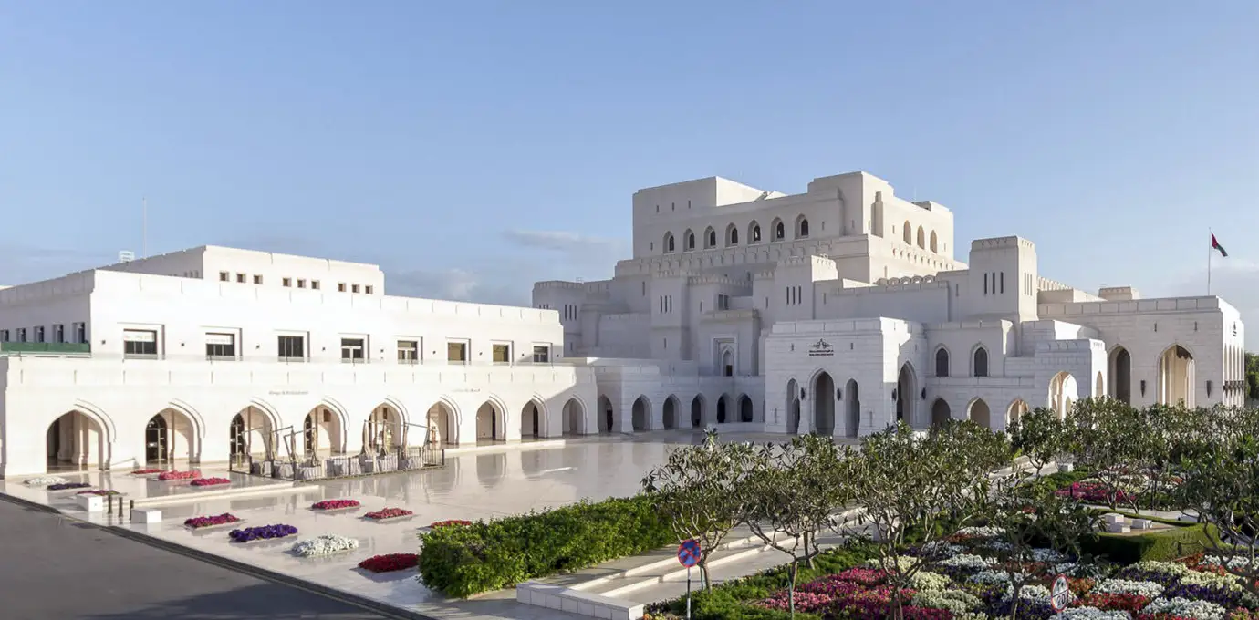 Royal Opera House Muscat exterior with white marble architecture, arches, and landscaped gardens under a clear sky.