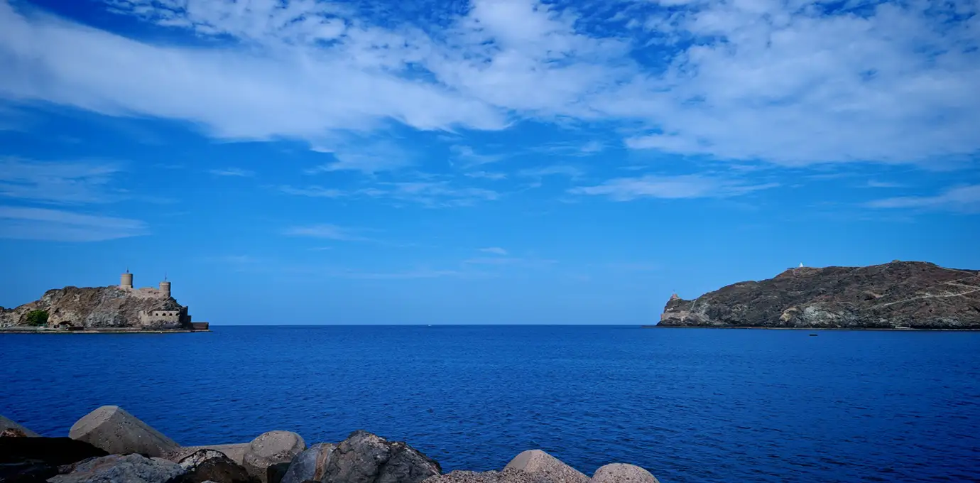 Blue coastal waters and rocky cliffs near Sur, Oman, under a bright sky.