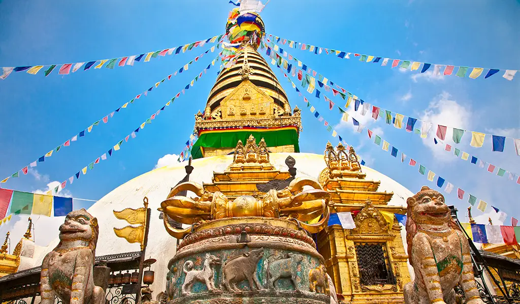 A close-up view of Swayambhunath Stupa in Kathmandu, Nepal, with a white dome, golden spire, colorful prayer flags, and guardian statues.