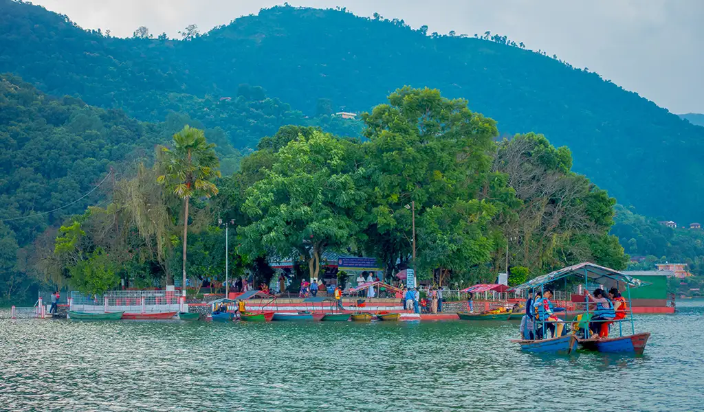 Boats carry visitors across Phewa Lake to Tal Barahi Temple, a small island shrine in Pokhara, Nepal, with forested hills behind.
