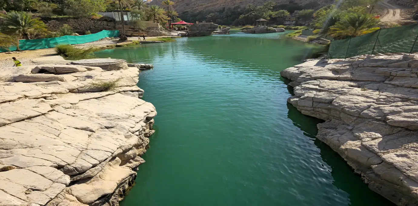 See the lear emerald pool surrounded by rocky cliffs at Wadi Bani Khalid in Oman during Oman Highlight Tour.
