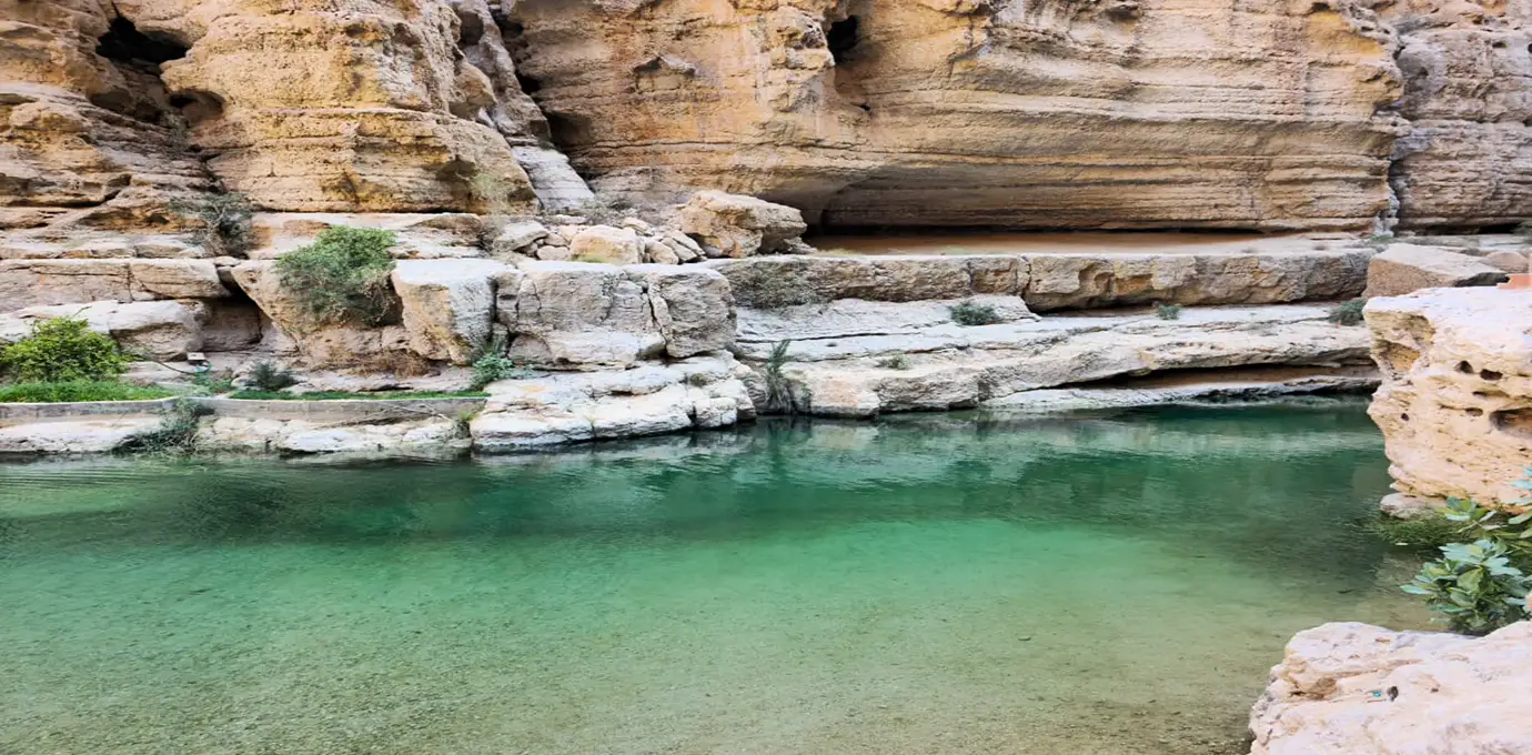 Clear turquoise pool surrounded by rocky cliffs at Wadi Shab in Oman.
