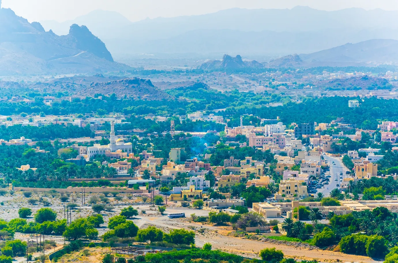 Aerial view of Al Hamra town in Oman, surrounded by greenery and rugged mountains.