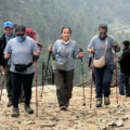 Three trekkers using hiking poles walk along a rugged stone trail accompanied by their private guide to the Everest Base Camp Trek in the forested Khumbu region.