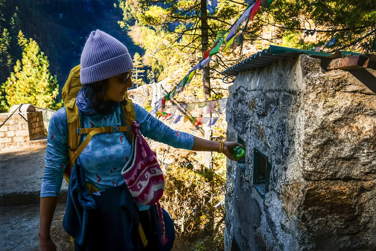 Trekker beside a stone wall and prayer flags on the Everest trail, showing a quiet stop during Everest Base Camp altitude sickness prevention and acclimatization.