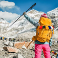 Trekker standing at Everest Base Camp with snowy peaks, prayer flags, and a trekking pole, showing the harsh high-altitude setting linked to Everest Base Camp altitude sickness prevention.