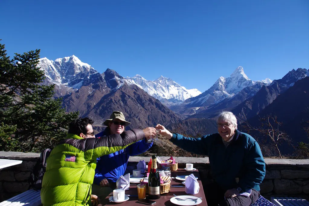 Travelers enjoying breakfast with a champagne toast at a mountain lodge terrace overlooking Mount Everest and surrounding Himalayan peaks during a luxury Everest Base Camp trek.