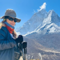 A female trekker equipped with hiking poles and gear stands before the towering Ama Dablam peak, illustrating the Everest Base Camp trek fitness level required for high-altitude Himalayan terrain.