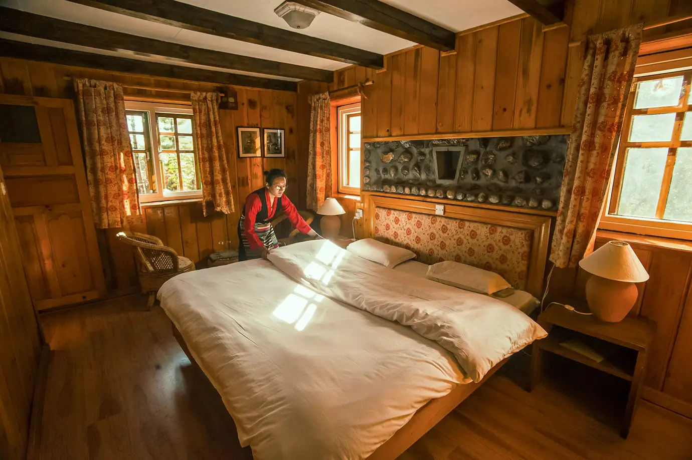 A lodge staff member preparing a comfortable wooden guest room at a mountain lodge in the Everest region of Nepal.