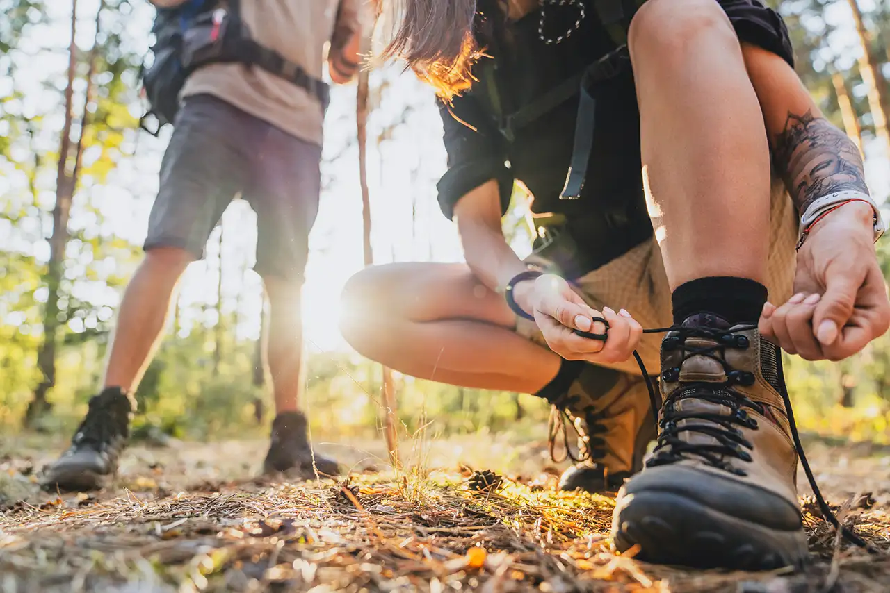 Hiker tying trekking boots on a forest trail before starting a hiking or trekking adventure.
