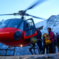 Travelers board a red helicopter in the Himalayas during a Luxury Nepal Tour Cost experience, with snow-covered peaks rising behind them.