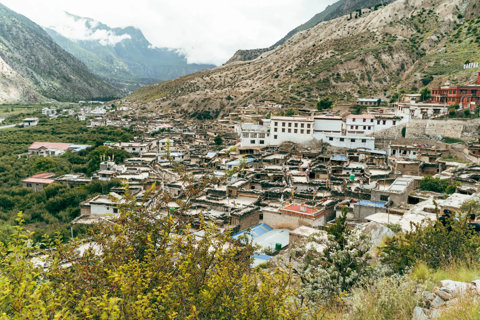 Traditional Marpha village in Mustang with white stone houses, narrow lanes, and surrounding hills under a cloudy sky.