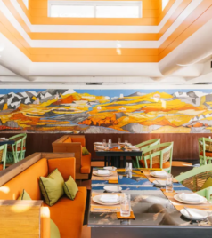 Modern restaurant with colorful mural, neatly arranged tables, and bright natural lighting.